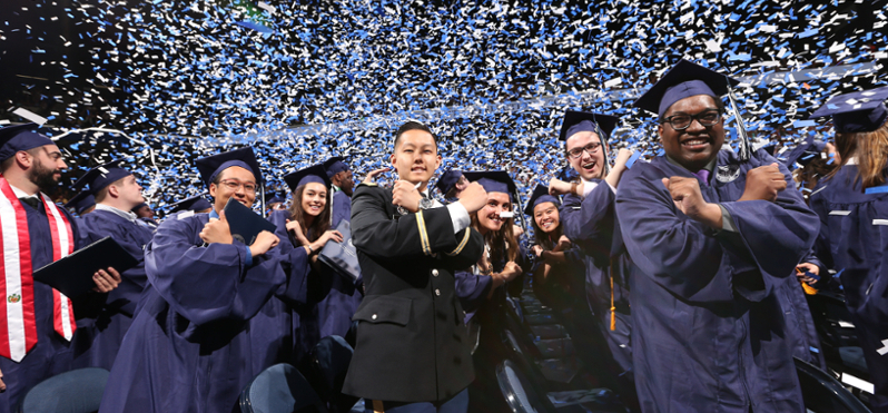 A row of Xavier students during graduation. They are crossing their arms to form an X. One student is in military uniform, the others are wearing traditional blue commencement gowns and caps.