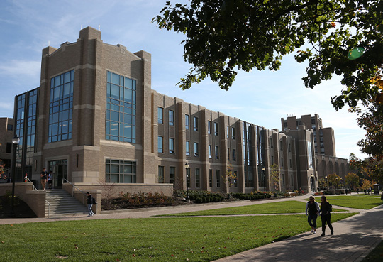 The exterior of Alter Hall on a sunny summer day on Xavier's campus. Two students wearing backpacks are walking on the sidewalk surrounding Alter.