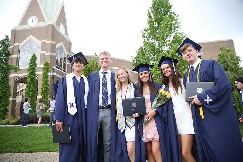 Six Xavier students outside of Gallagher Student Center celebrating commencement. They are all wearing their navy blue commencement robes.