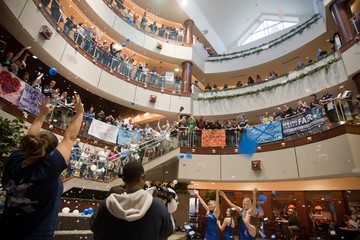 The interior atrium of Gallagher Student Center. Four floors are visible in the photo. Many students are cheering while standing on the floors.