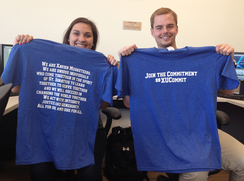 Two students holding blue t-shirts with Xavier's Student Commitment written on them