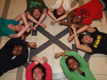 group of Xavier students laying in a circle on top of an X logo, all making the 'x' symbol by crossing their arms 