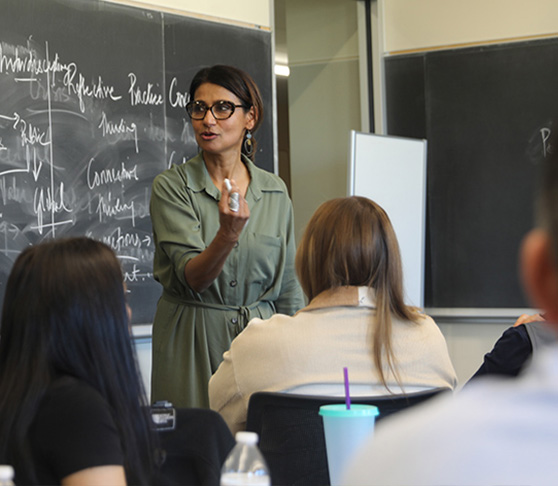 A Xavier professor leads a classroom in front of a chalkboard covered in writing.