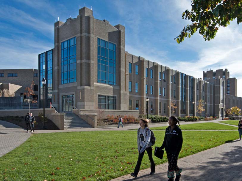 Two students walking outside Alter Hall on a sunny day.