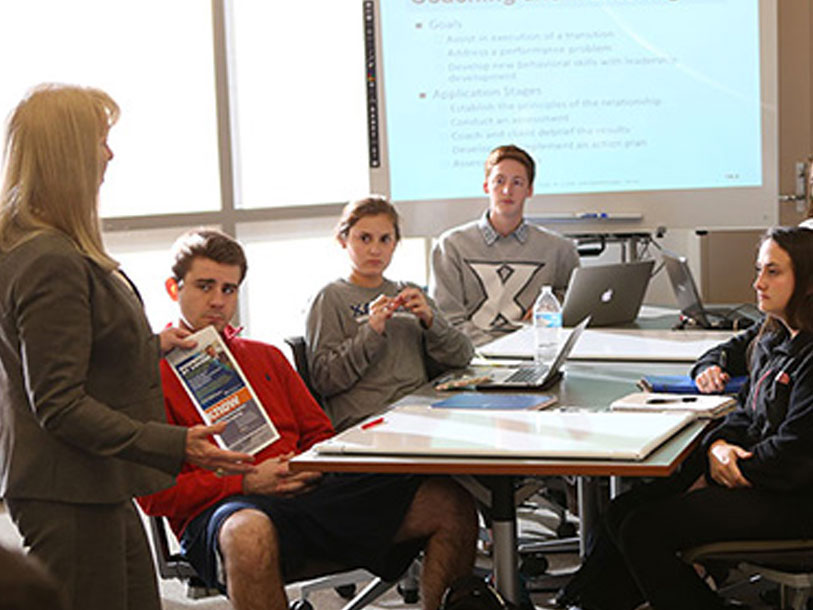 Four students sit at a table while an instructor shows them something on a sheet of paper.