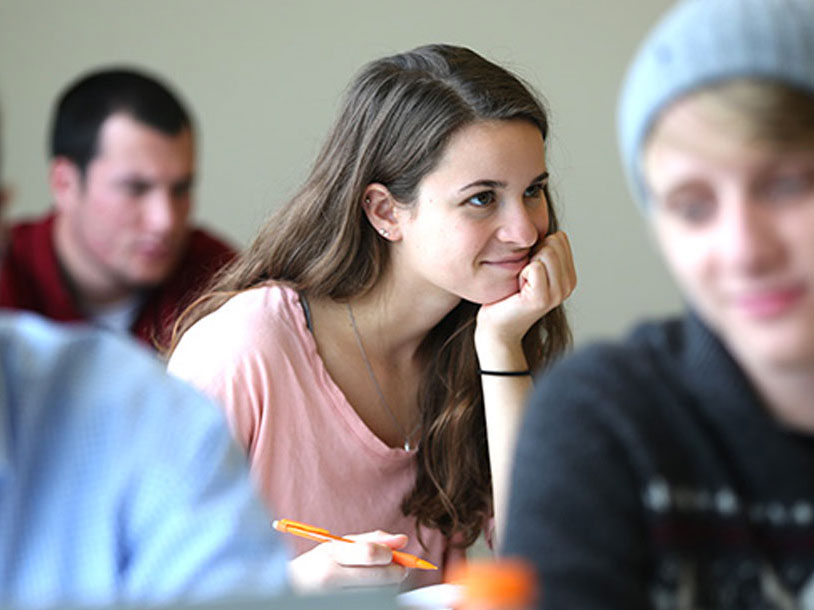 A student is at a desk resting their chin on the palm of their left hand.