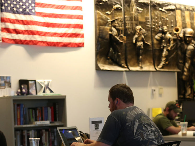 A student studying in the Veteran and Military Family Center. There is an American Flag in the background.