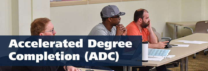 Three adult learners sitting at a desk in a classroom. Text reads: Accelerated Degree Completion (ADC)