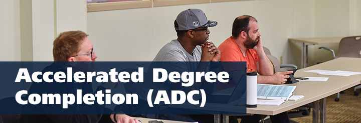 Three adult learners sitting at a desk in a classroom. Text reads: Accelerated Degree Completion (ADC)