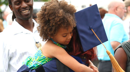 Xavier graduate in their cap and gown hugging a small child