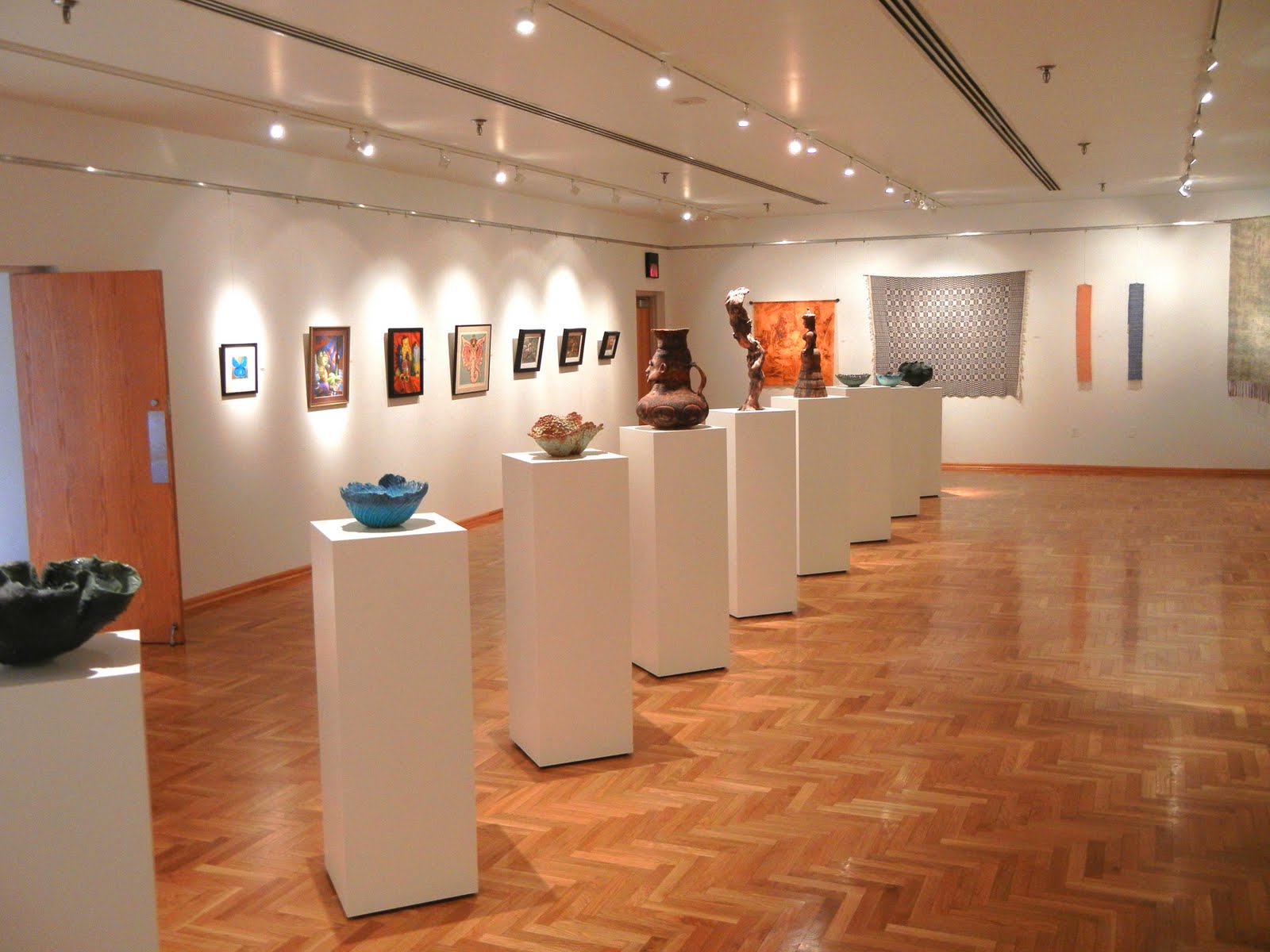Photo of the interior of the AB Cohen Center art gallery. Paintings hang on the wall and ceramic art rests on pedestals.