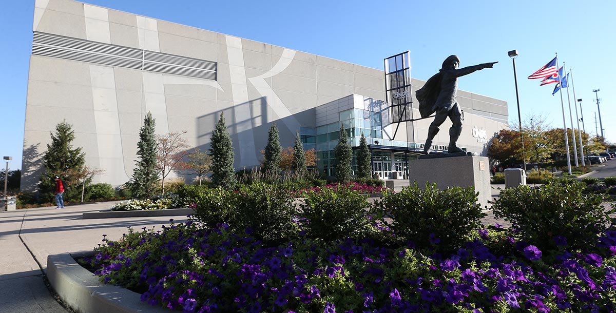 Exterior of the Cintas Center on a spring day. There is a D'Artagnan statue and flowers in front of the building.
