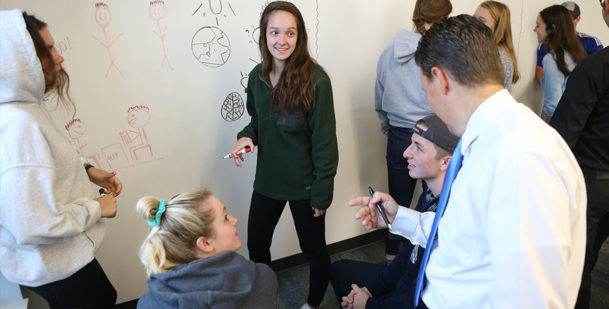 Students writing on a white-board and smiling