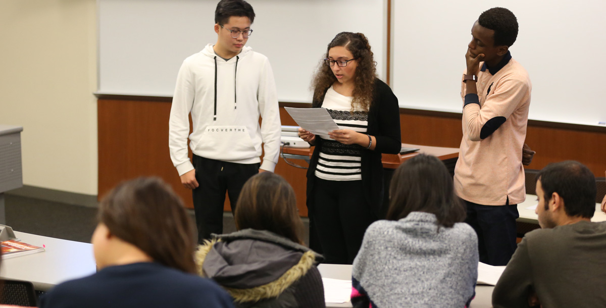 Three students presenting a paper to their class