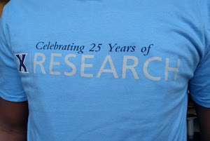 A student wearing a blue t-shirt. The text on the shirt reads 'Celebrating 25 Years of Research'. There is a Xavier X logo to the left of the text.