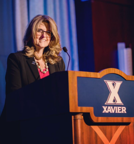 A photo of Xavier University President Colleen Hanycz behind a podium. She is smiling.
