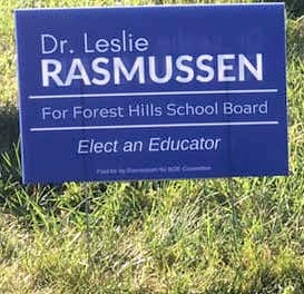 An election sign sticking out of a grassy lawn. The text on the political sign reads: Dr. Leslie Rasmussen for Forest Hills School Board. Elect an Educator'