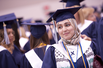 A Xavier graduate in their blue and white commencement cap and gown. The graduate is smiling.