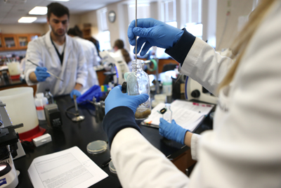 Photo of Students in Labcoats Conducting a Lab Experiment
