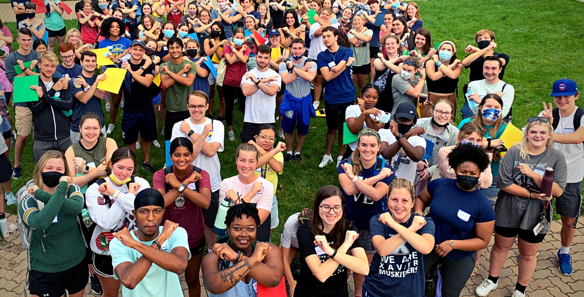 Group of ninety students outside holding up the X with their arms