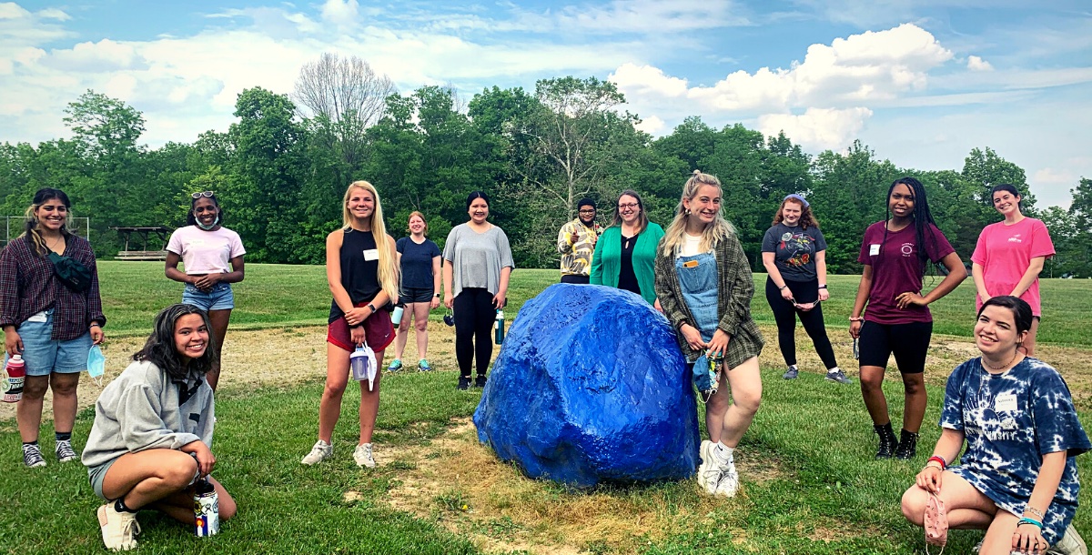 Group outdoors spread out around the Camp Joy rock on a sunny day