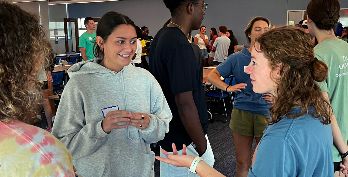 Three students in conversation in a room full of students