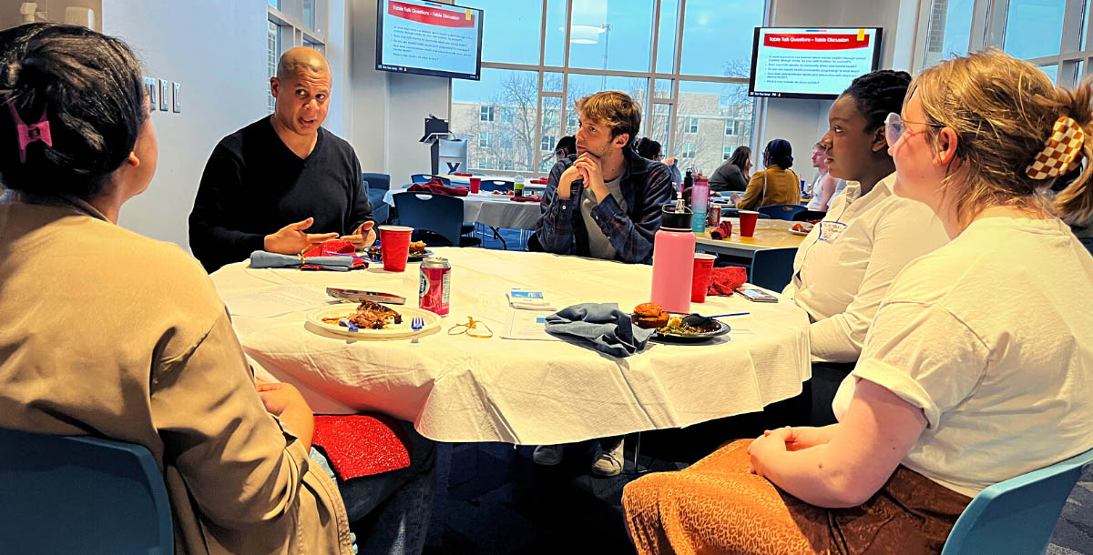 Table of students of varying races, genders, and beliefs in serious conversation