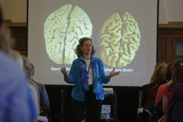 Nursing professor lecturing inside a classroom with the picture of a brain on a projector, right behind her
