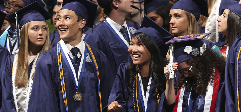 Four Xavier students in their blue caps and gowns smiling during their commencement ceremony