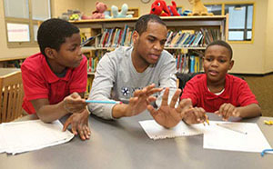 Xavier student helping two younger boys sitting at a classroom table