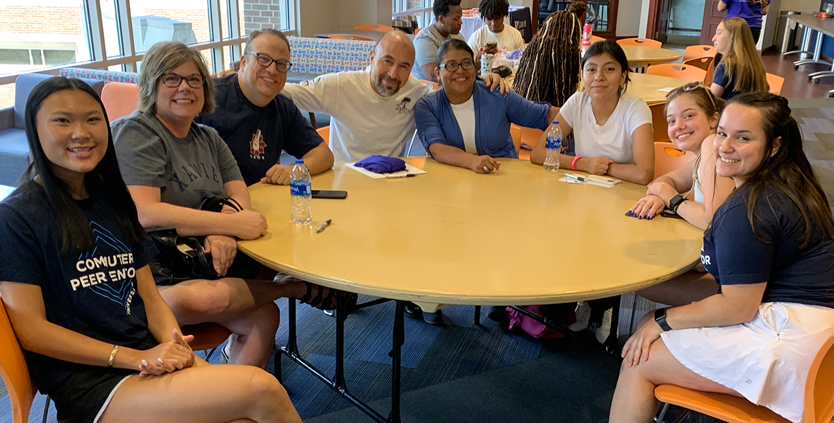 A group of eight students and staff sitting at a table and smiling