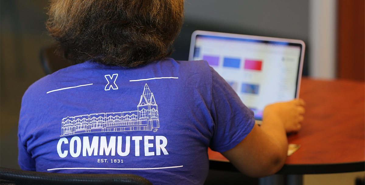 A photo of the back of a student's purple tee-shirt says 'Commuter' under a drawing of Gallagher Student Center. In white text.