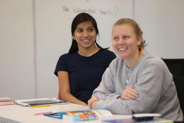 Two students sitting at desks in a classroom. They are both smiling.