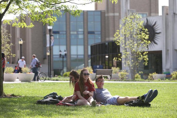 Three Xavier students leaning against each other under the shade of a tree