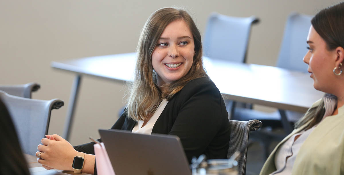 An adult student smiles in conversation with another adult student.