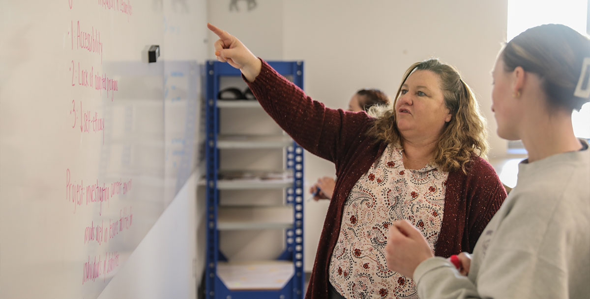 A professor points to the whiteboard while speaking with a student