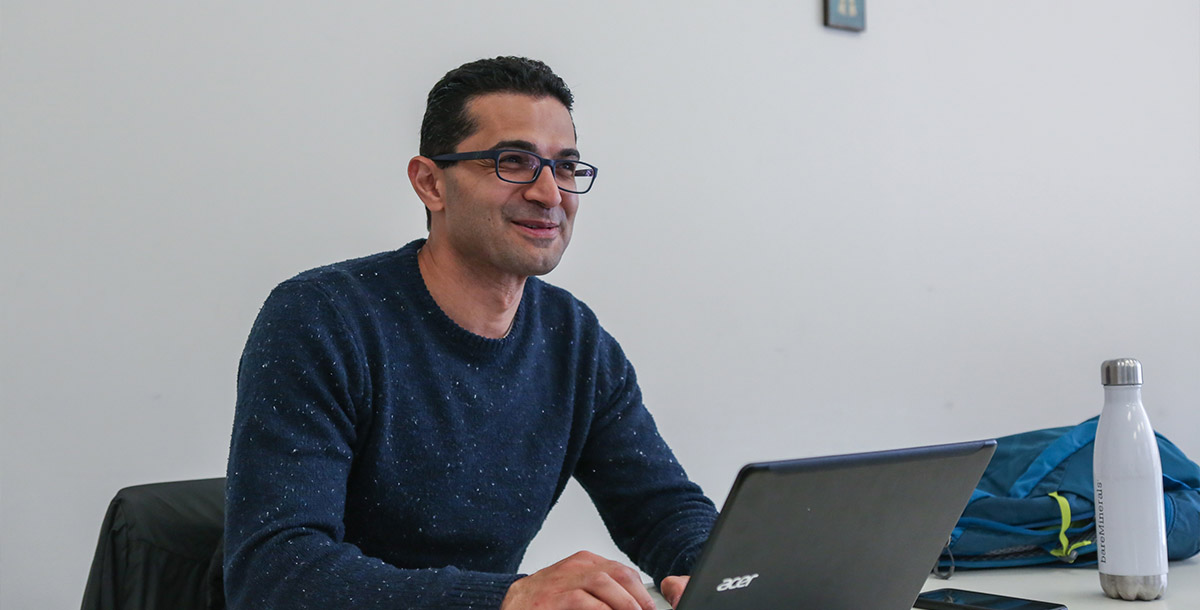 Adult student sitting at a desk and smiling. There is an open laptop in front of him.