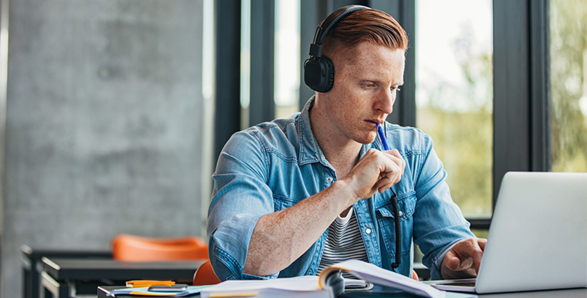 A student wears headphones while working on a laptop