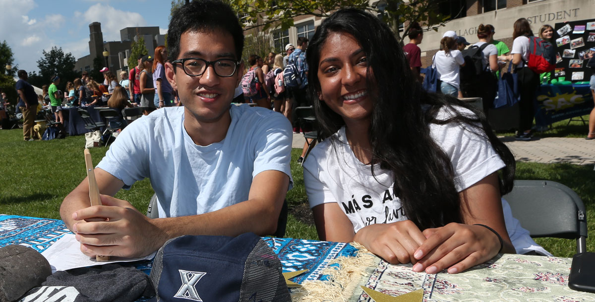 Two students sit together at a table during the annual Club Day. They are both smiling at the camera.