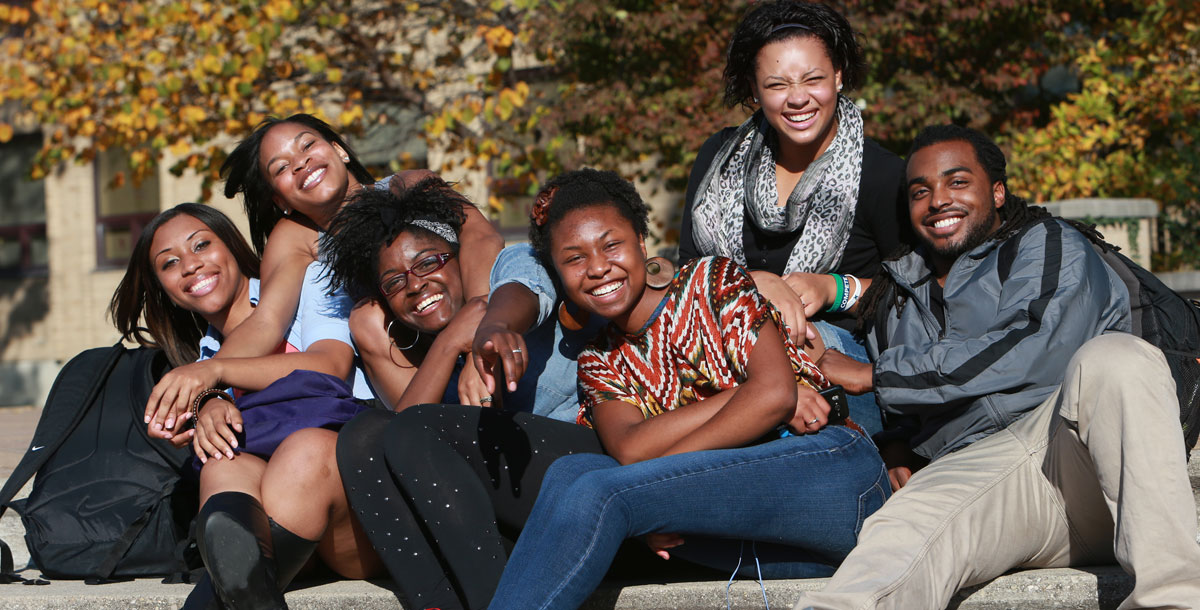 Six students sitting outside together on a fall day. They are all close together and smiling at the camera.