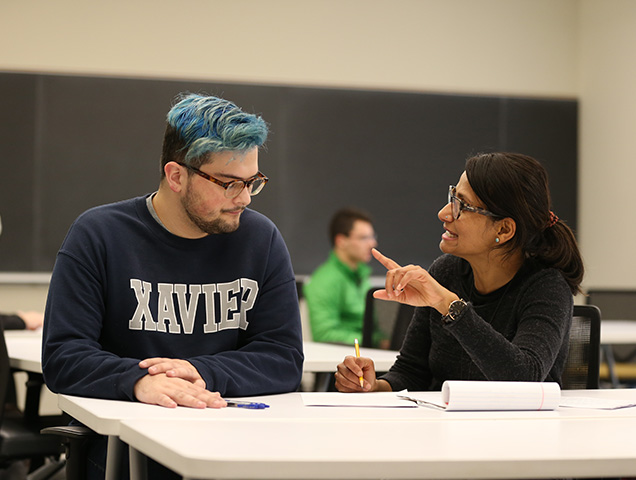 Economics major sitting at a desk speaking to a professor who is sitting beside them.