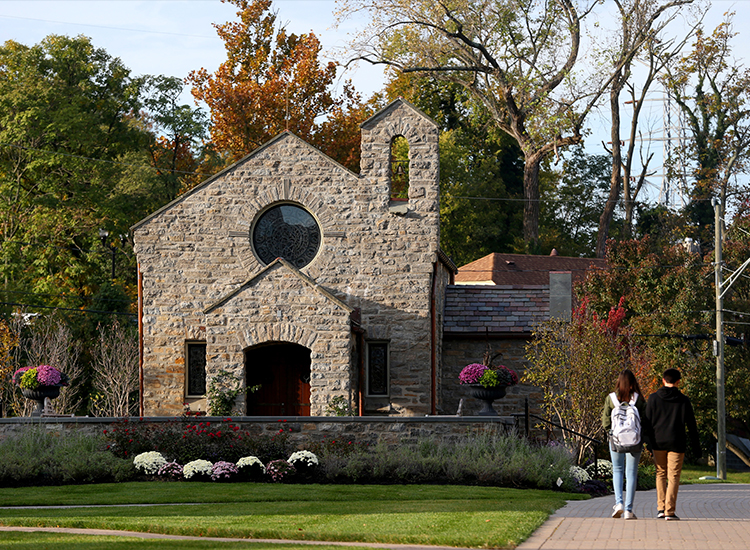 Two students walk toward Dana Avenue, passing Our Lady of Peace Chapel