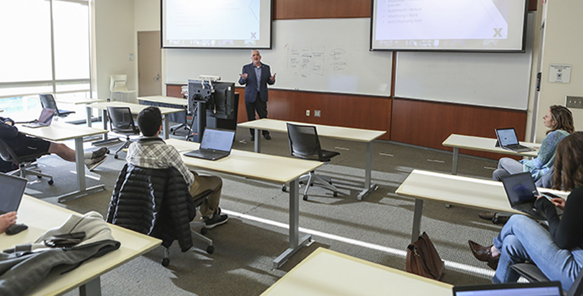 A professor leading a classroom of students in front of a whiteboard. 