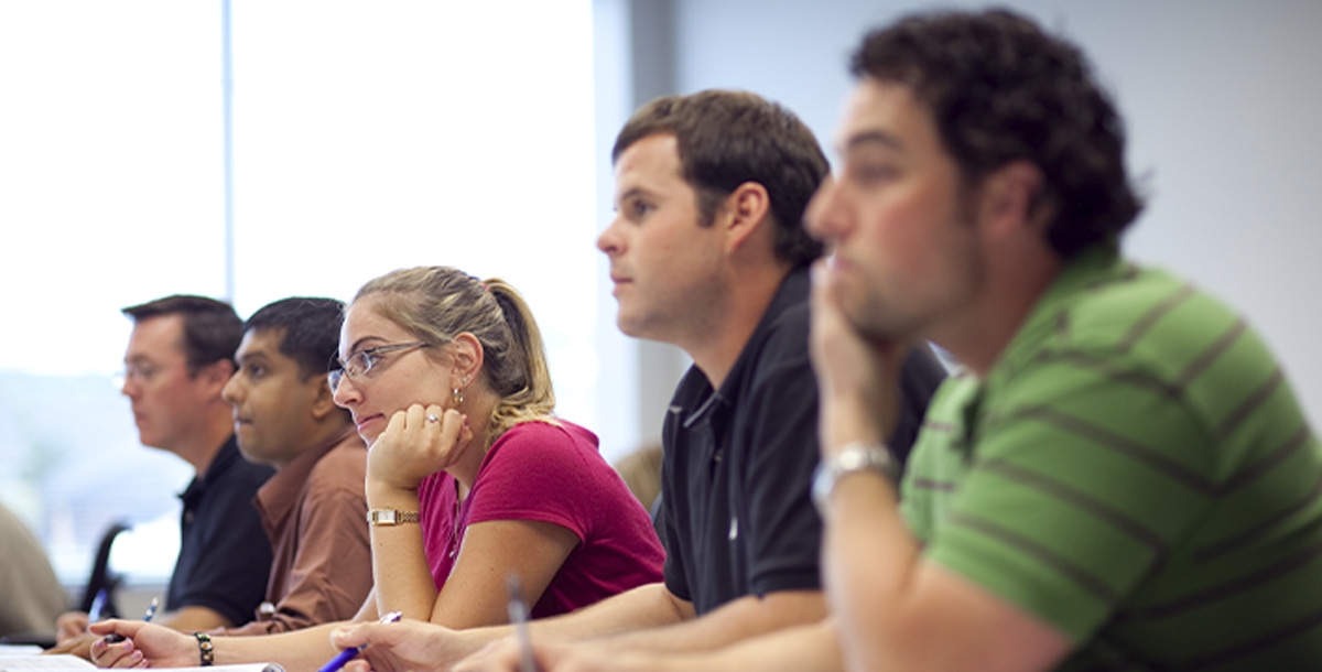 Five students sitting in a row at a long desk. The photo is of their profiles. 