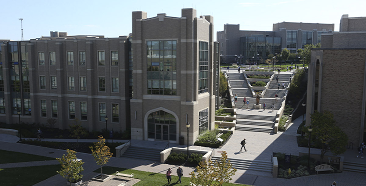 Exterior of Alter Hall on campus on a sunny summer day. Students are walking down the Ignatian steps beside the building. 