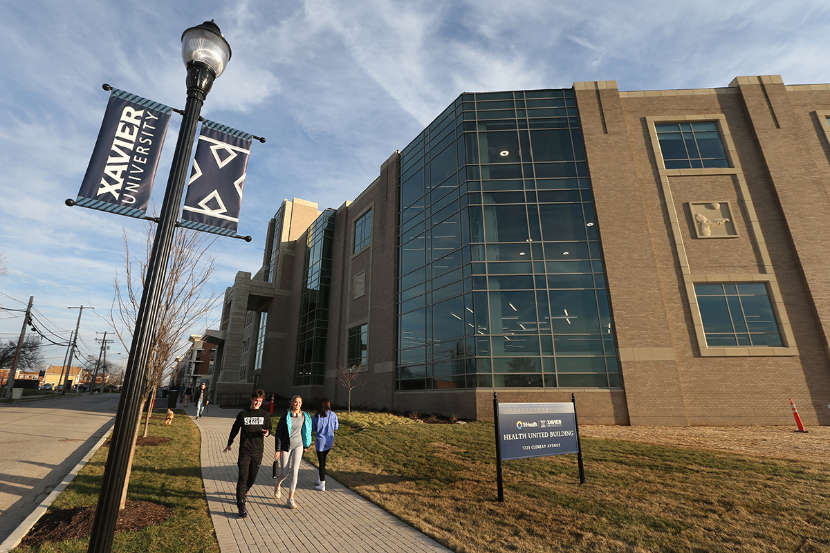 Three students walking on a sidewalk outside the Health United Building on an overcast day