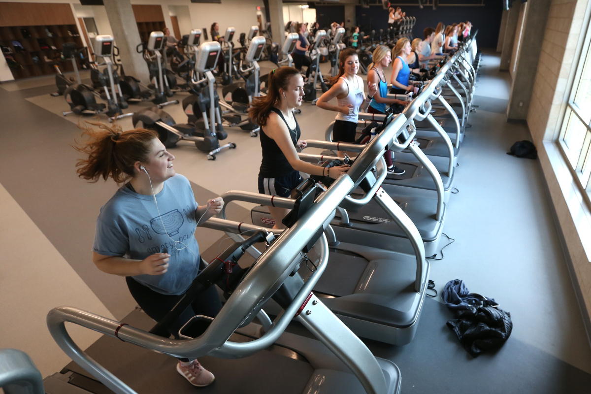 Students running on a row of treadmills in the Health United Building. There are rows of exercise backs behind them.