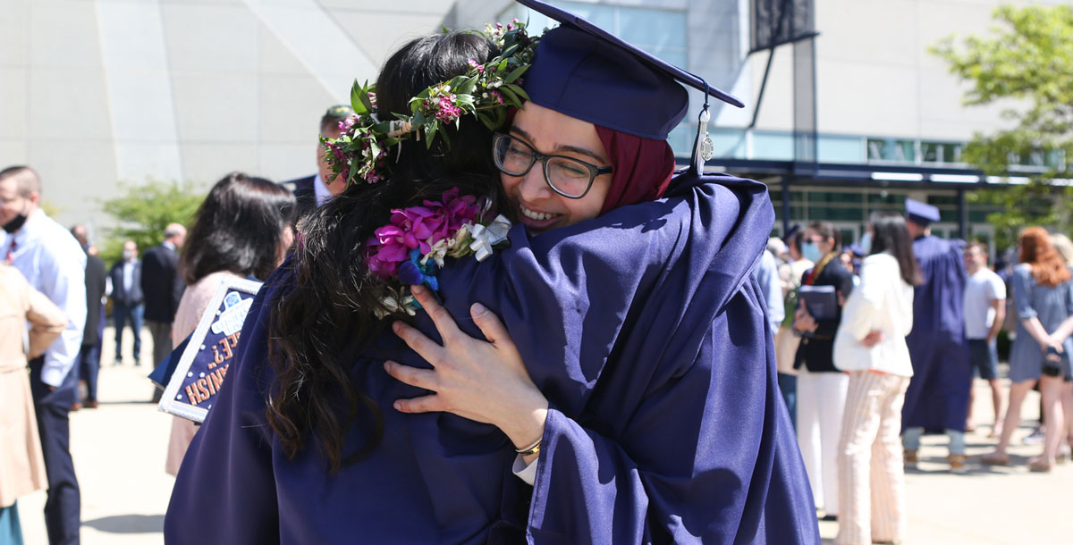 Two Xavier graduates hug on their graduation day. They are both wearing navy blue graduation caps and gowns.