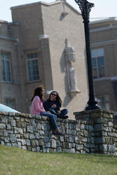 Two students sit on the stone wall in front of Hinkle Hall. They are in conversation.