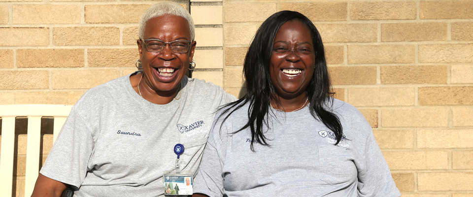 Two Xavier employees smiling together on a bench on campus